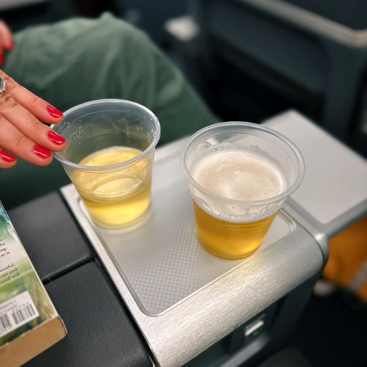 Two plastic cups of beer on an American Airlines tray table