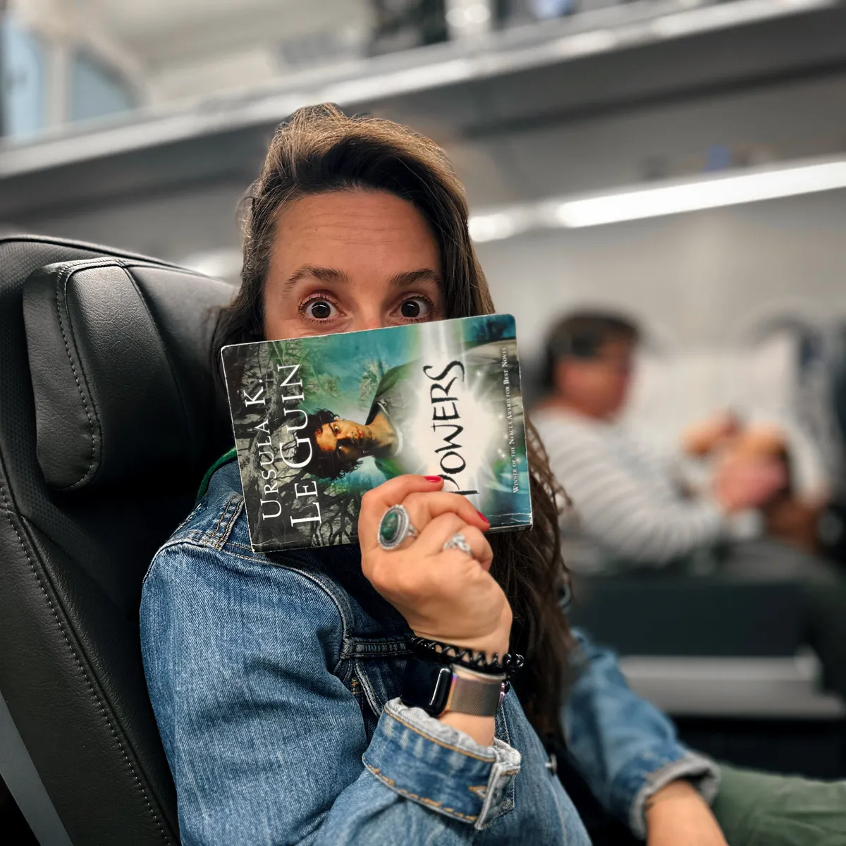 Passenger holding Ursula K Le Guin's Powers in an airplane seat