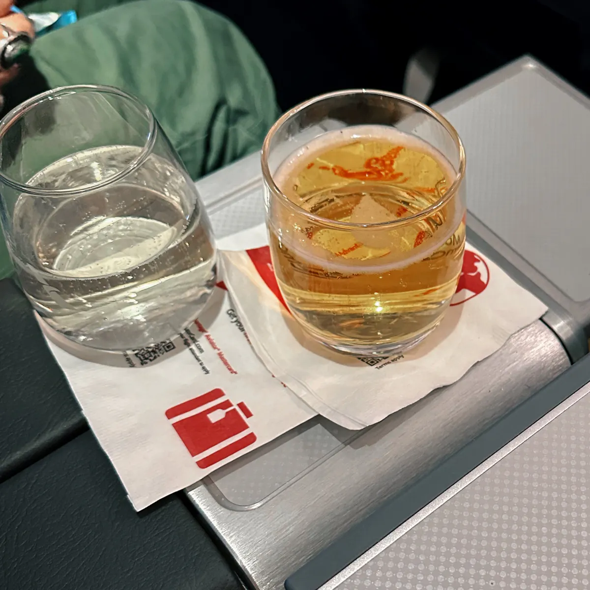 Glasses of water and a foamy drink on an airline napkin