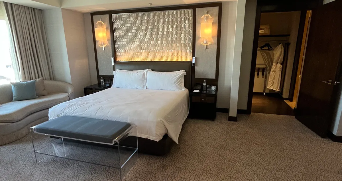 Large hotel bed with a metallic headboard, sofa, and open closet