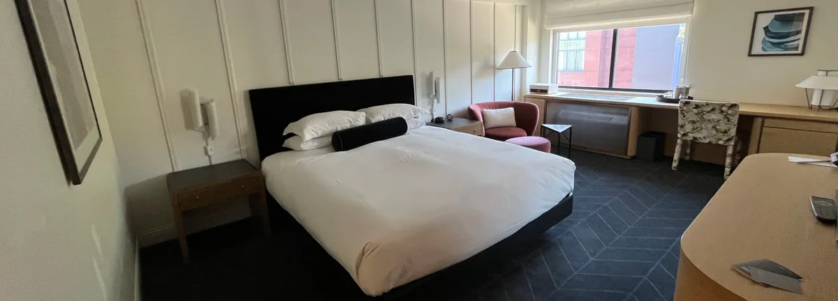Modern hotel room with a white bed, black headboard, and desk