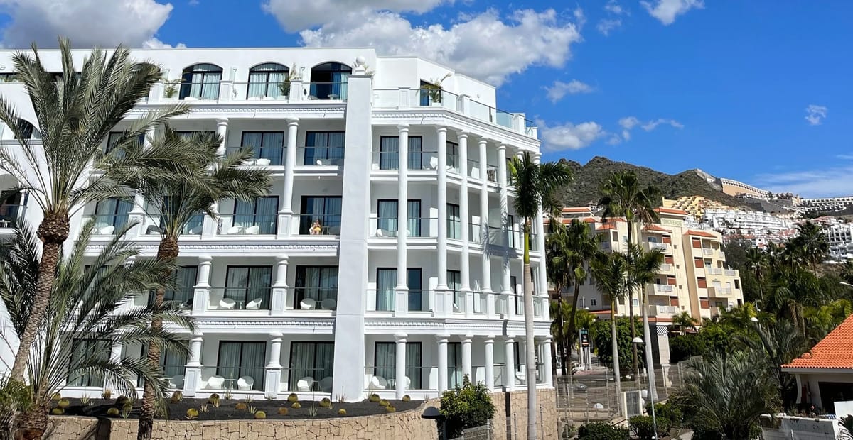 White columned hotel with balconies and palms against a hillside