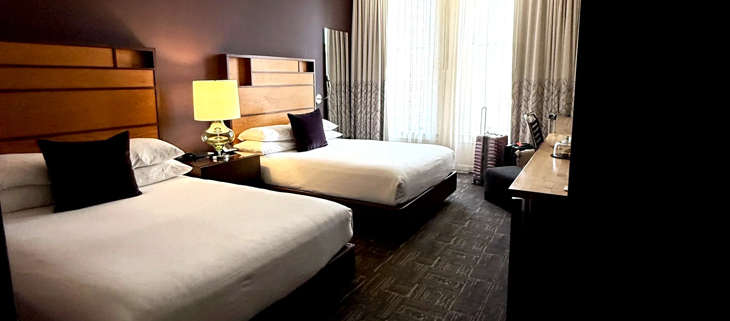 Hotel room with two beds, a lamp, and a suitcase by the window