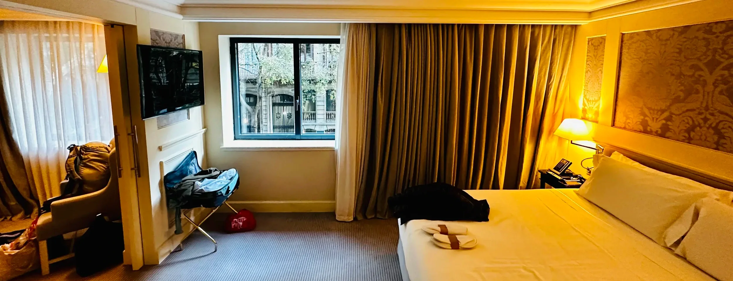 Hotel room with gold curtains, a large bed, and a wall-mounted television