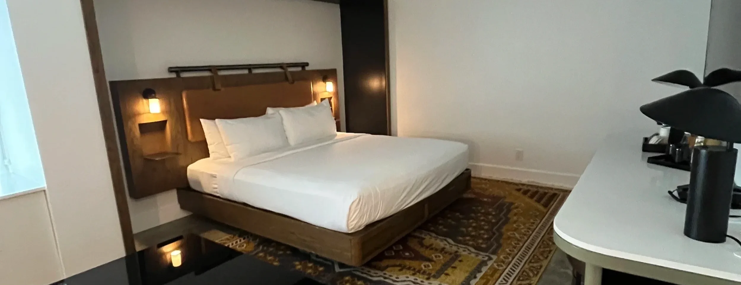 Hotel bedroom with a wood headboard, white bedding, and a desk