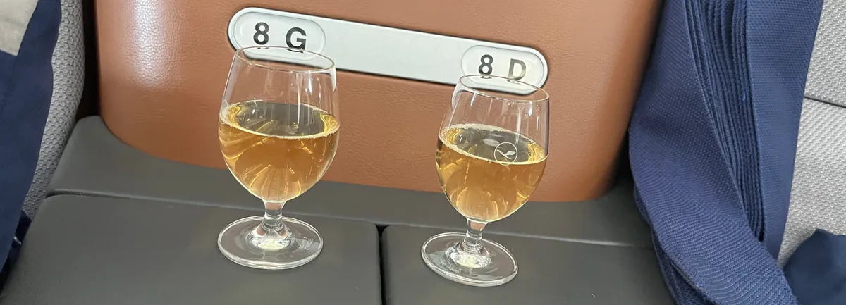 Two glasses of white wine on a Lufthansa console labeled 8G and 8D