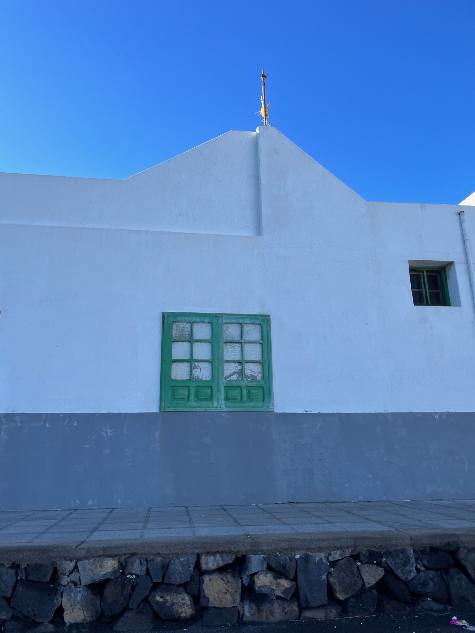 White gabled building with green shutters and a metal cross against a blue sky.