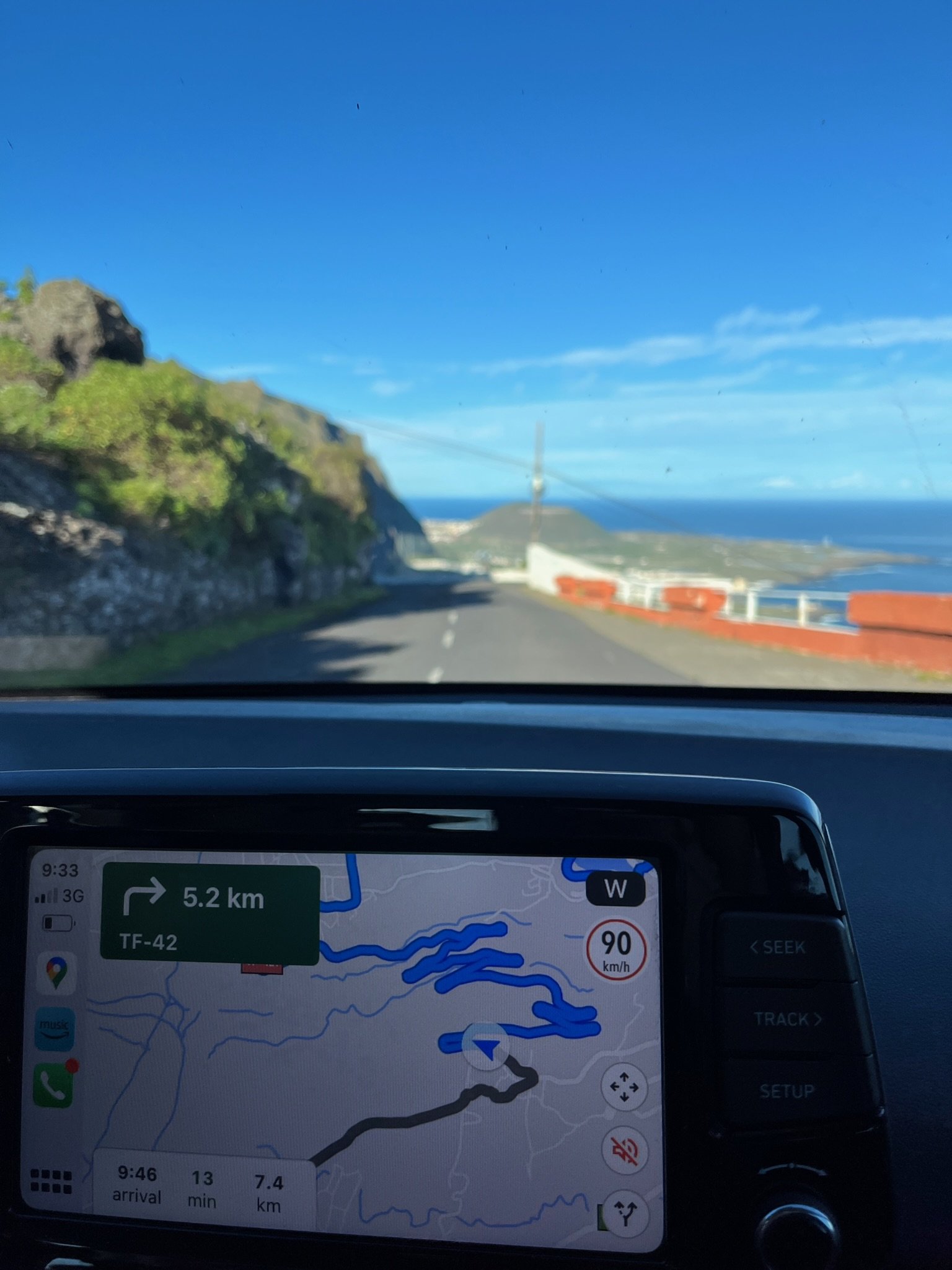 View through a windshield of a coastal road, with navigation on the dashboard.