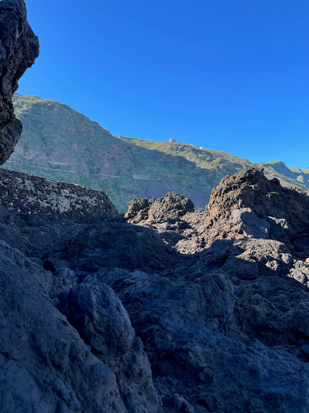 Jagged black lava rocks filling the foreground, with green mountains rising behind.