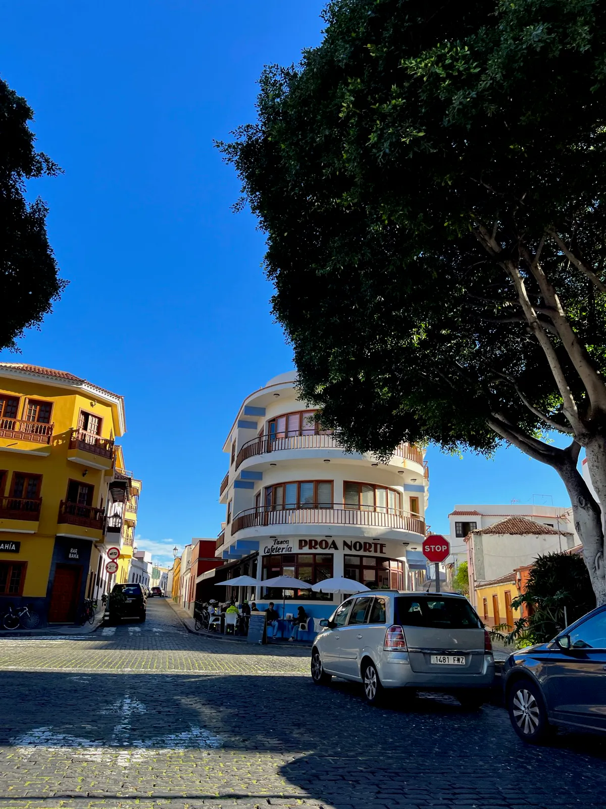 Cobblestone street lined with a yellow building and a curved cafe signed Proa Norte.