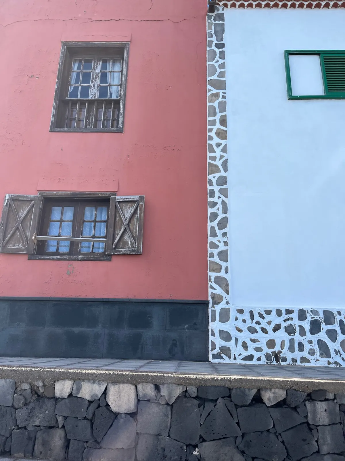 A salmon-pink wall with barred windows next to a white wall trimmed in stones.