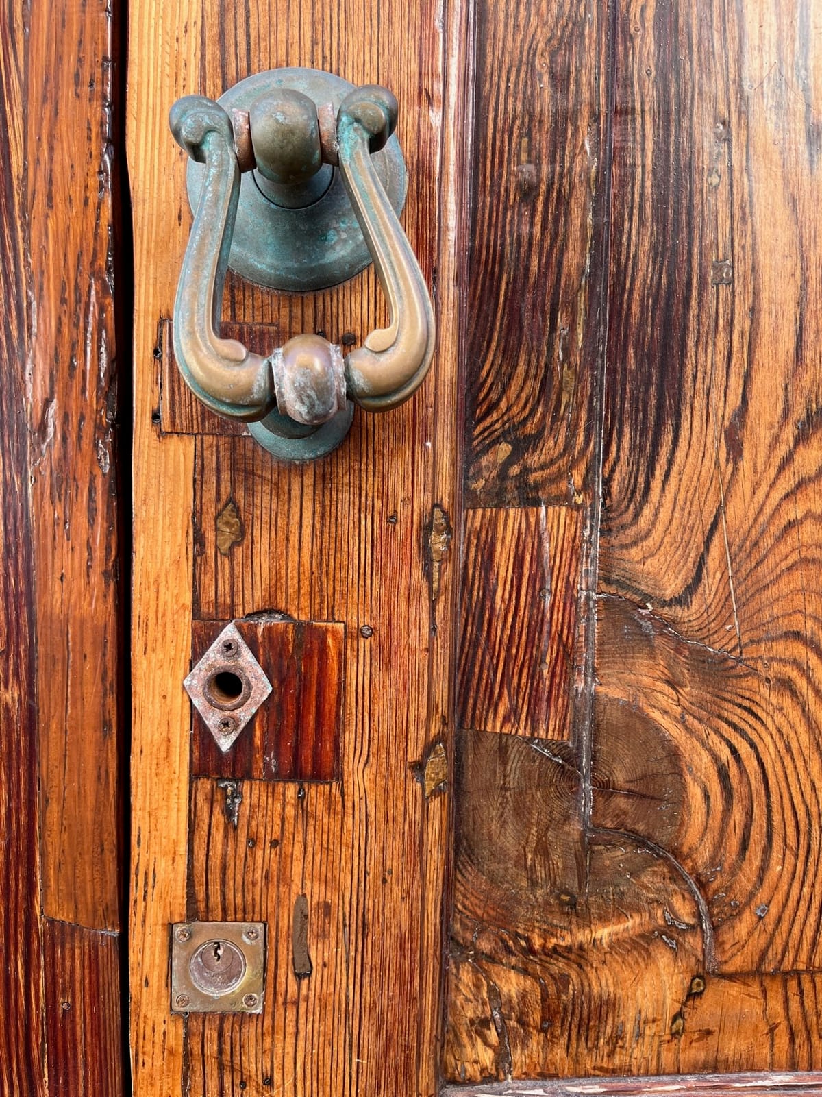 Weathered wooden door with a green brass knocker and two old keyholes.