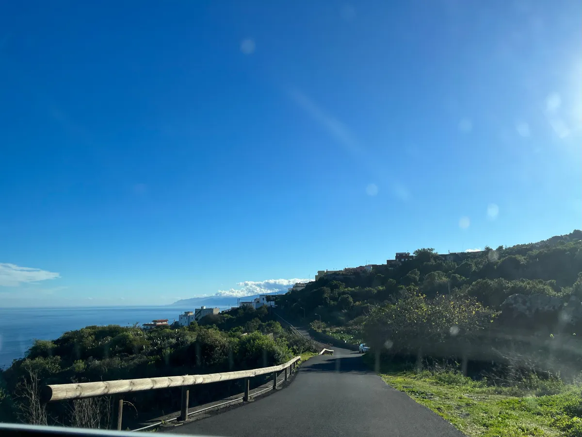 A winding hillside road past scattered white houses, with the ocean on the left.