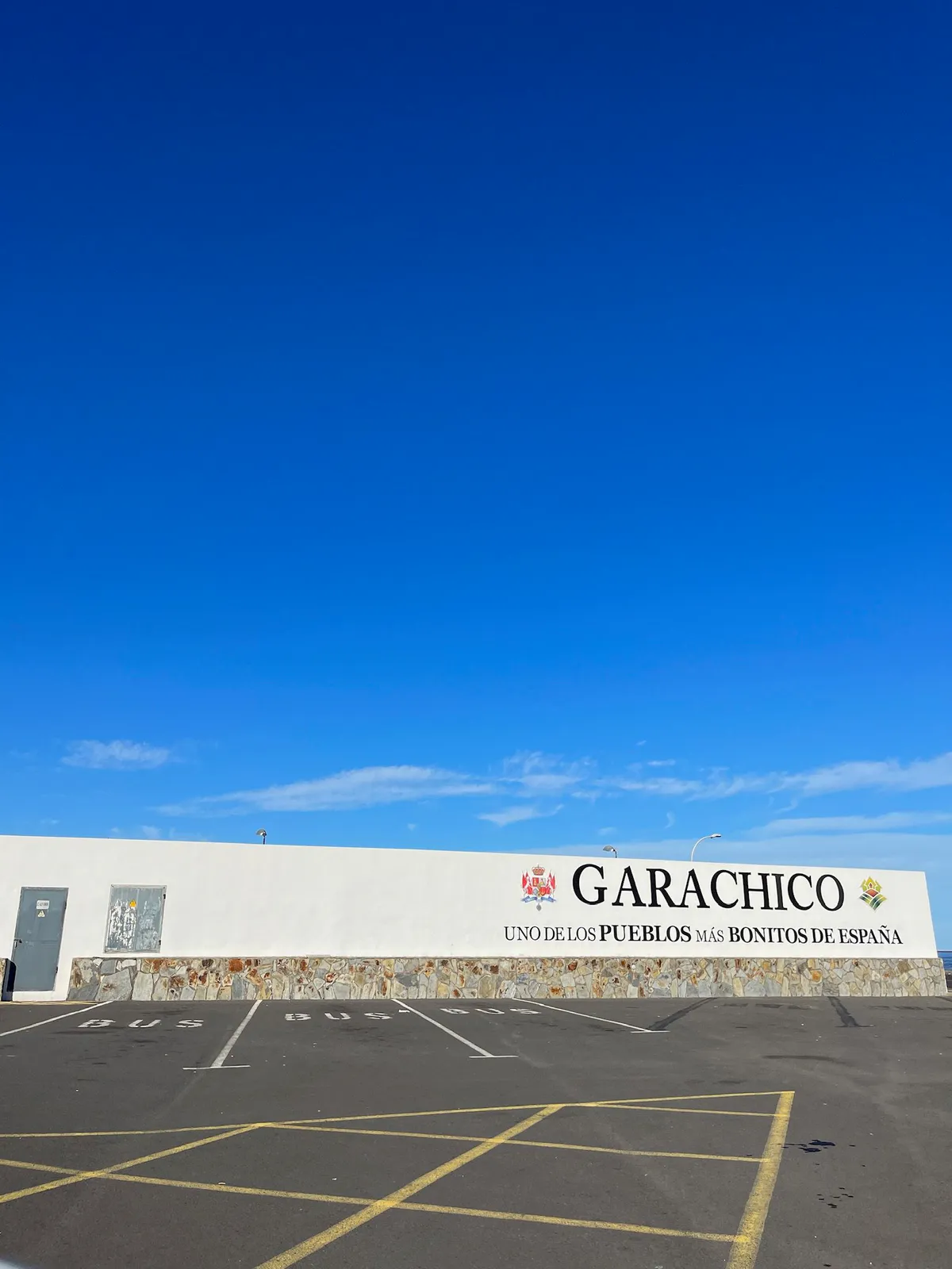 A long white wall lettered Garachico above empty bus parking spaces.