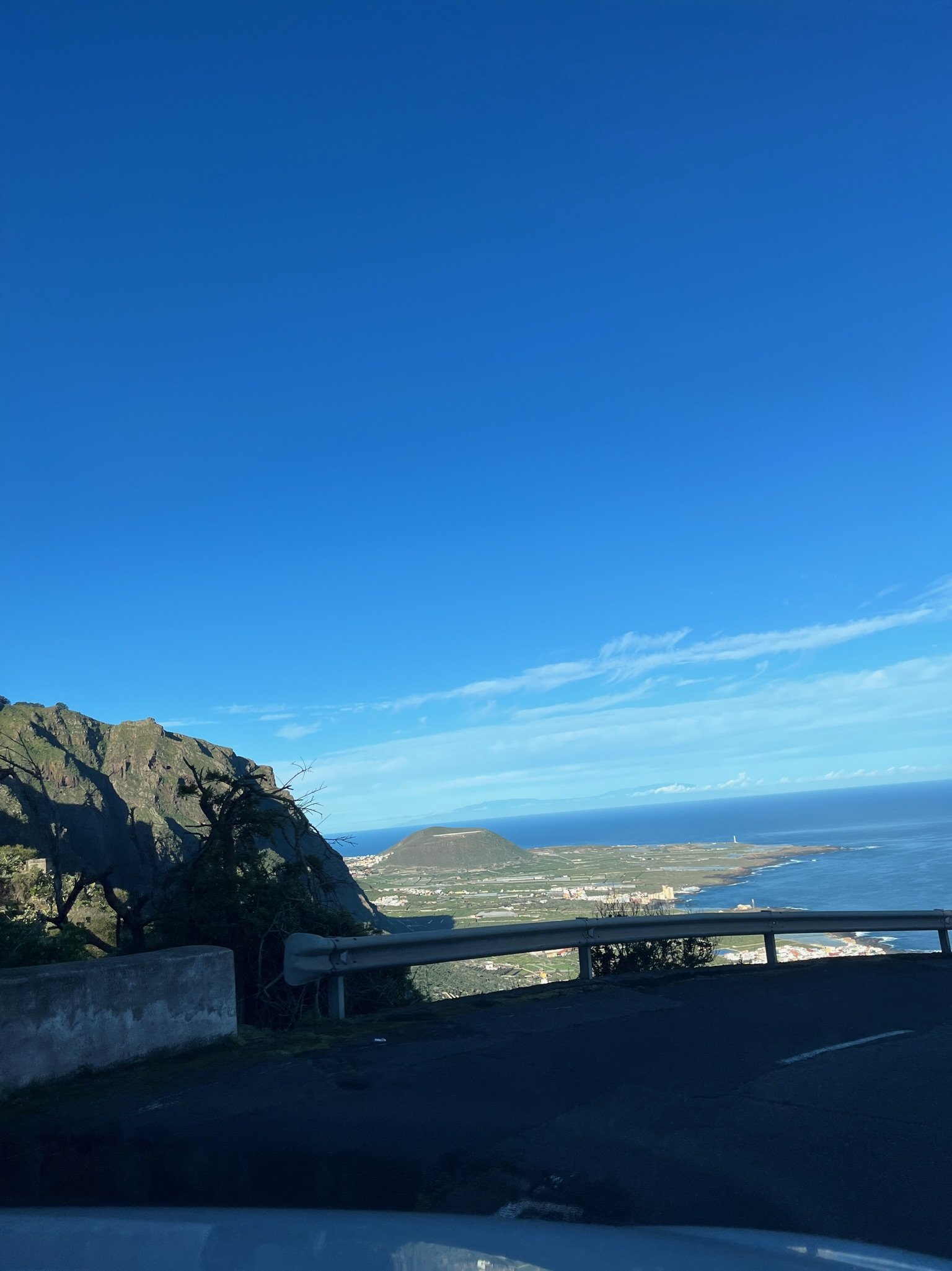 Cliffside overlook of a coastal town, a conical hill, and the open sea.