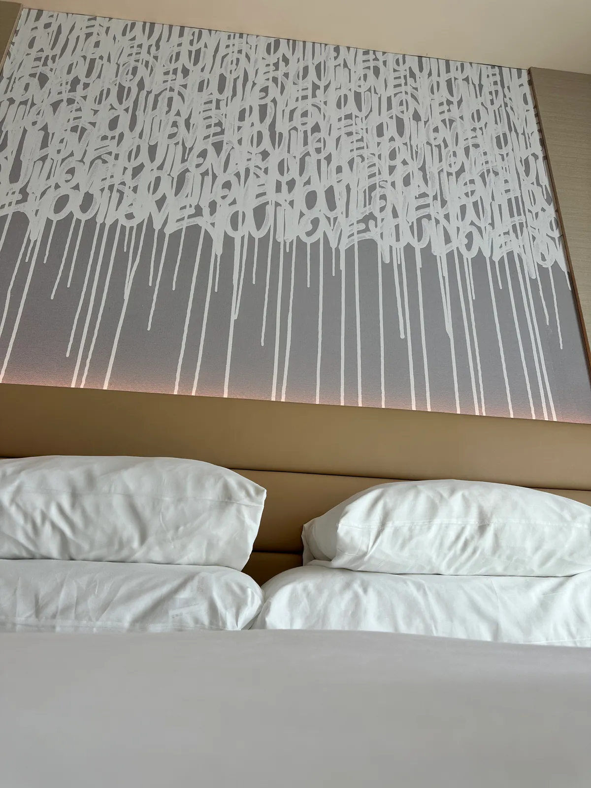 Close-up of four white pillows under dripping script art and a tan headboard