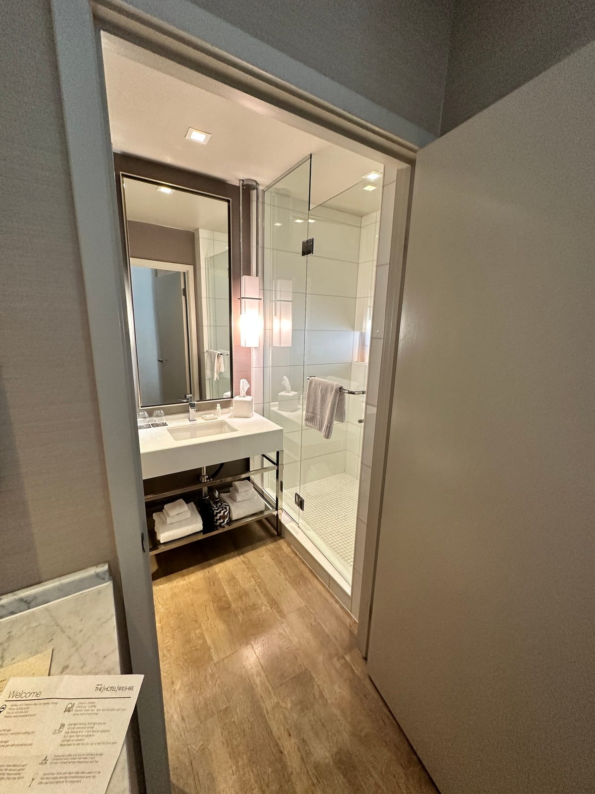 Doorway into a bathroom with a vanity, glass shower, and a welcome card