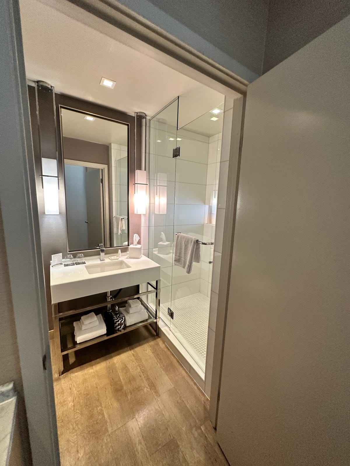 Bathroom vanity with stacked towels under a large mirror and a glass shower