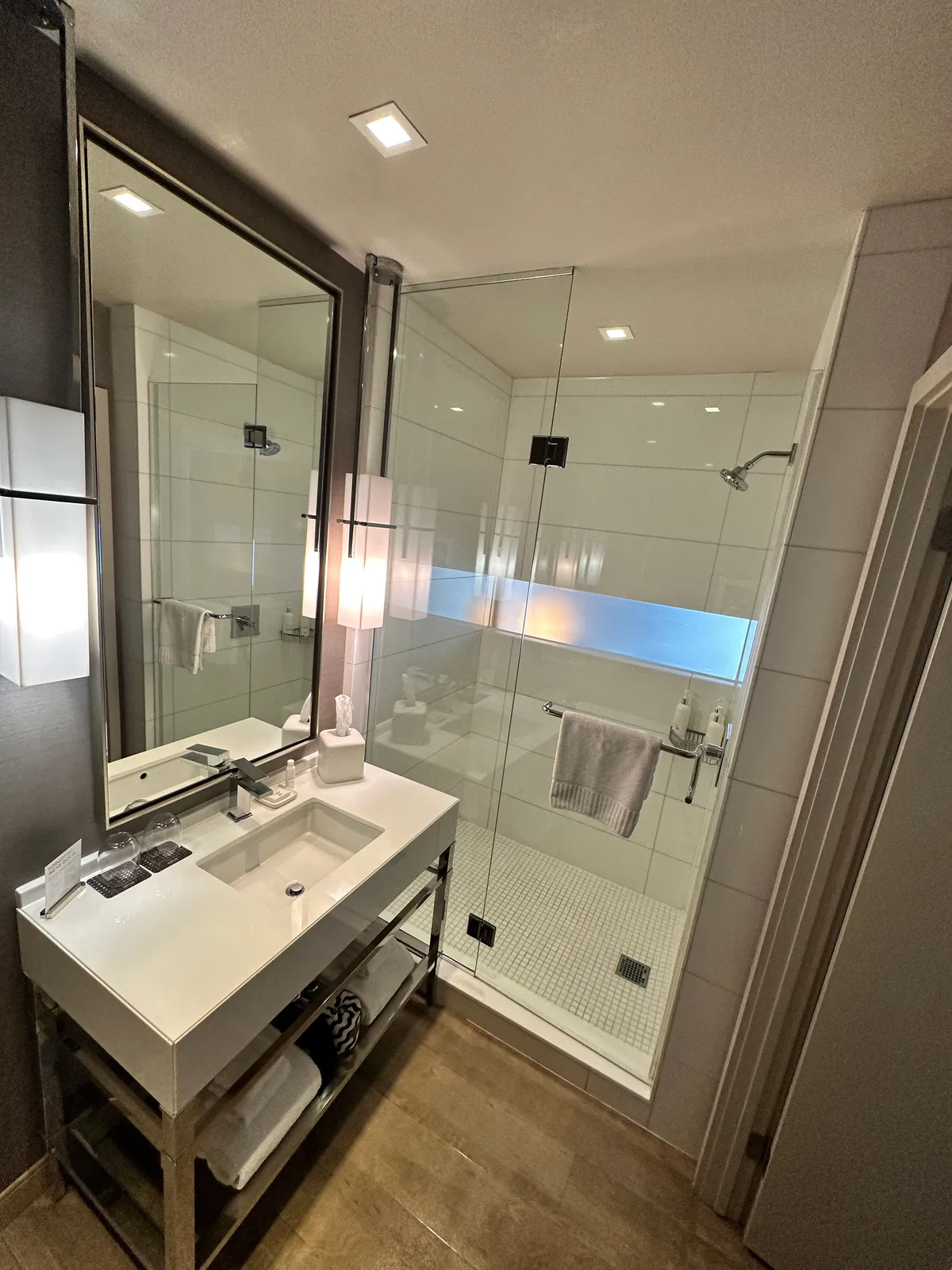White sink on a metal stand next to a glass shower with a blue band