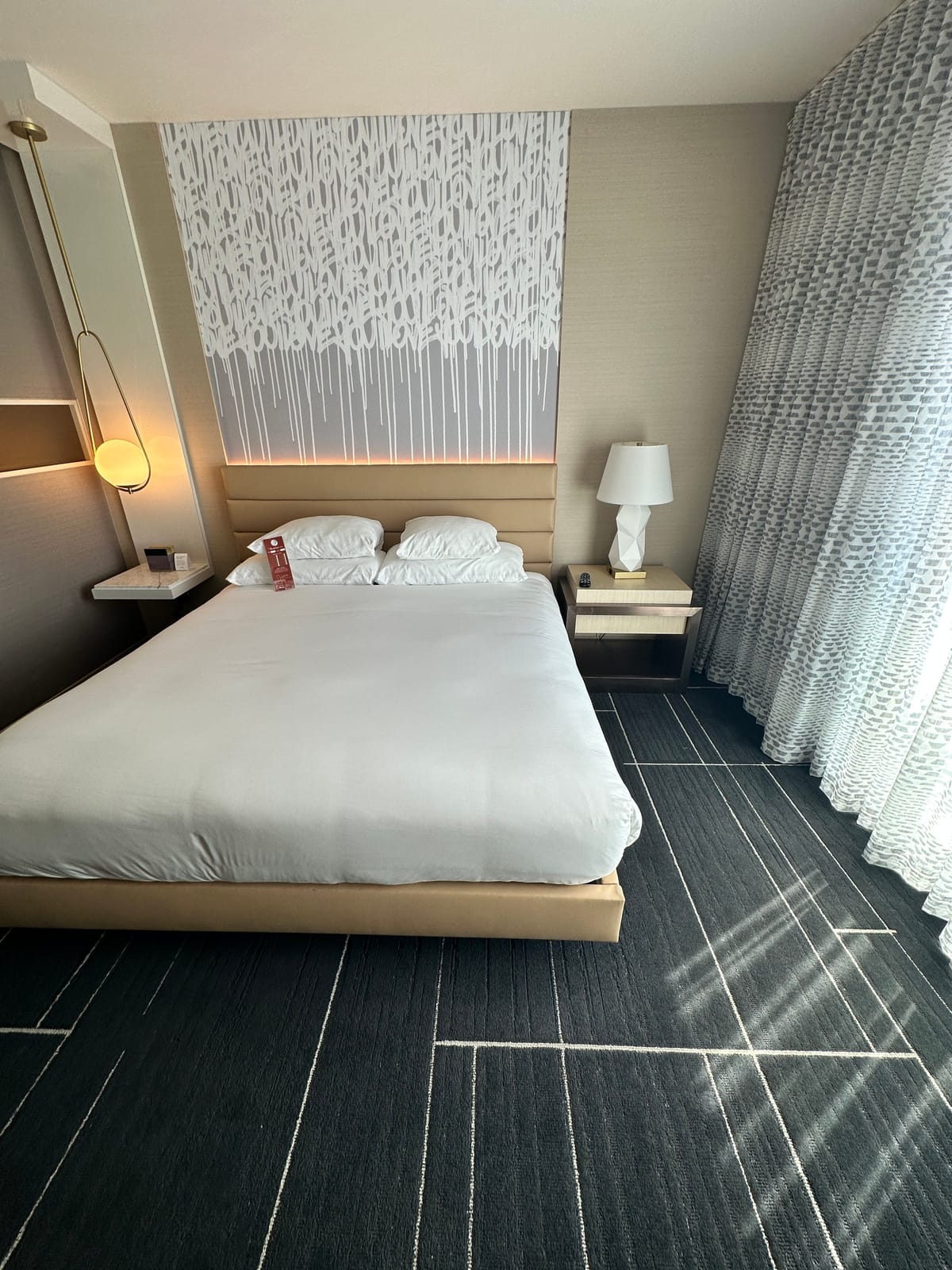 King bed in white linens under dripping wall art and patterned curtains
