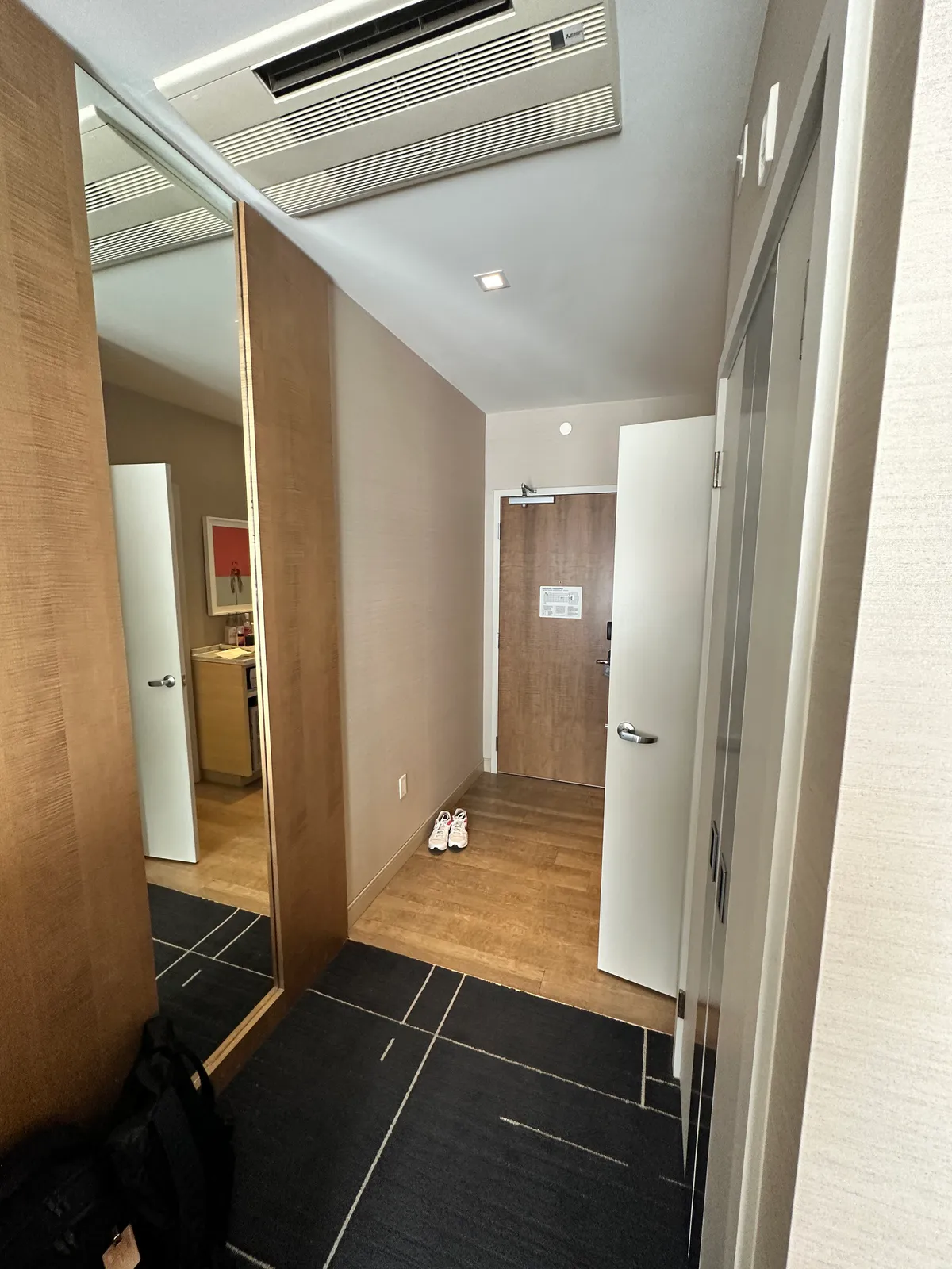 Room hallway toward a wood door, with shoes on the floor and a mirror
