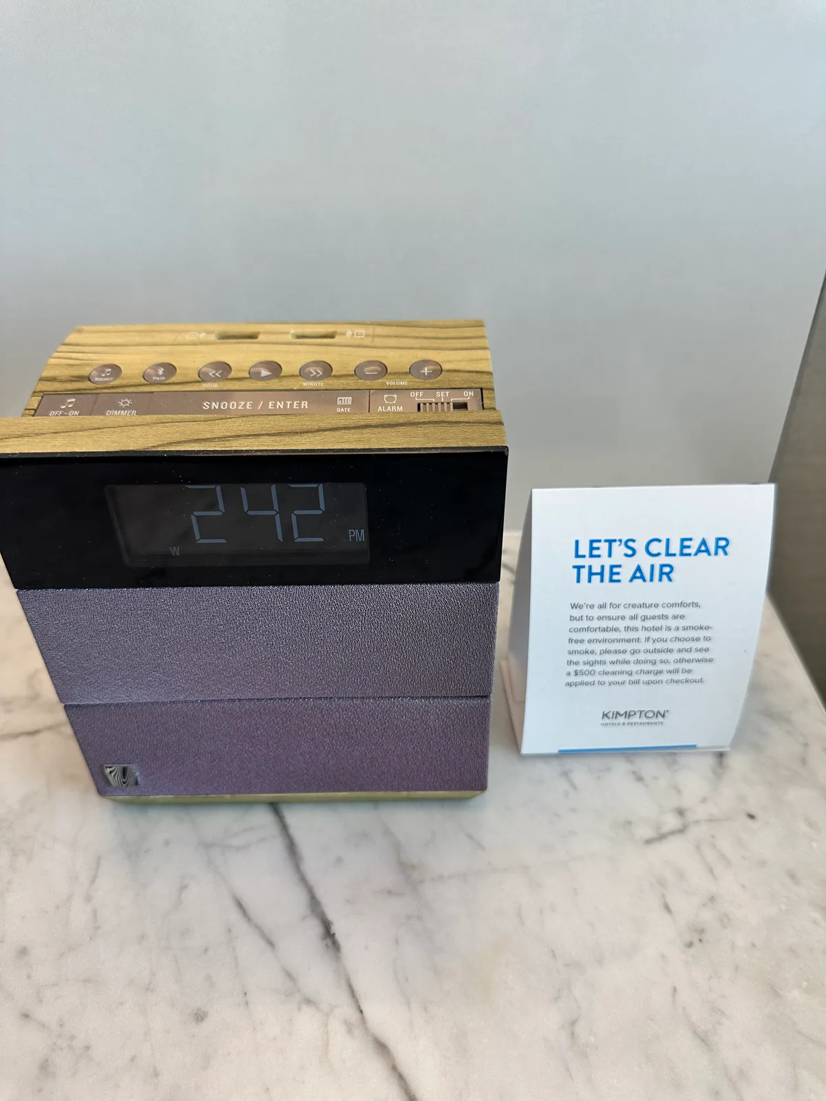 Alarm clock with a wood top beside a smoke-free notice on marble
