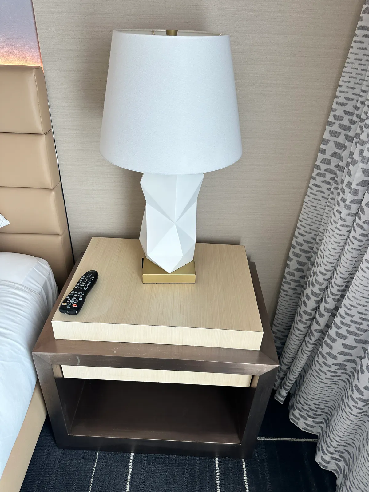 Bedside table holding a white geometric lamp and a black remote