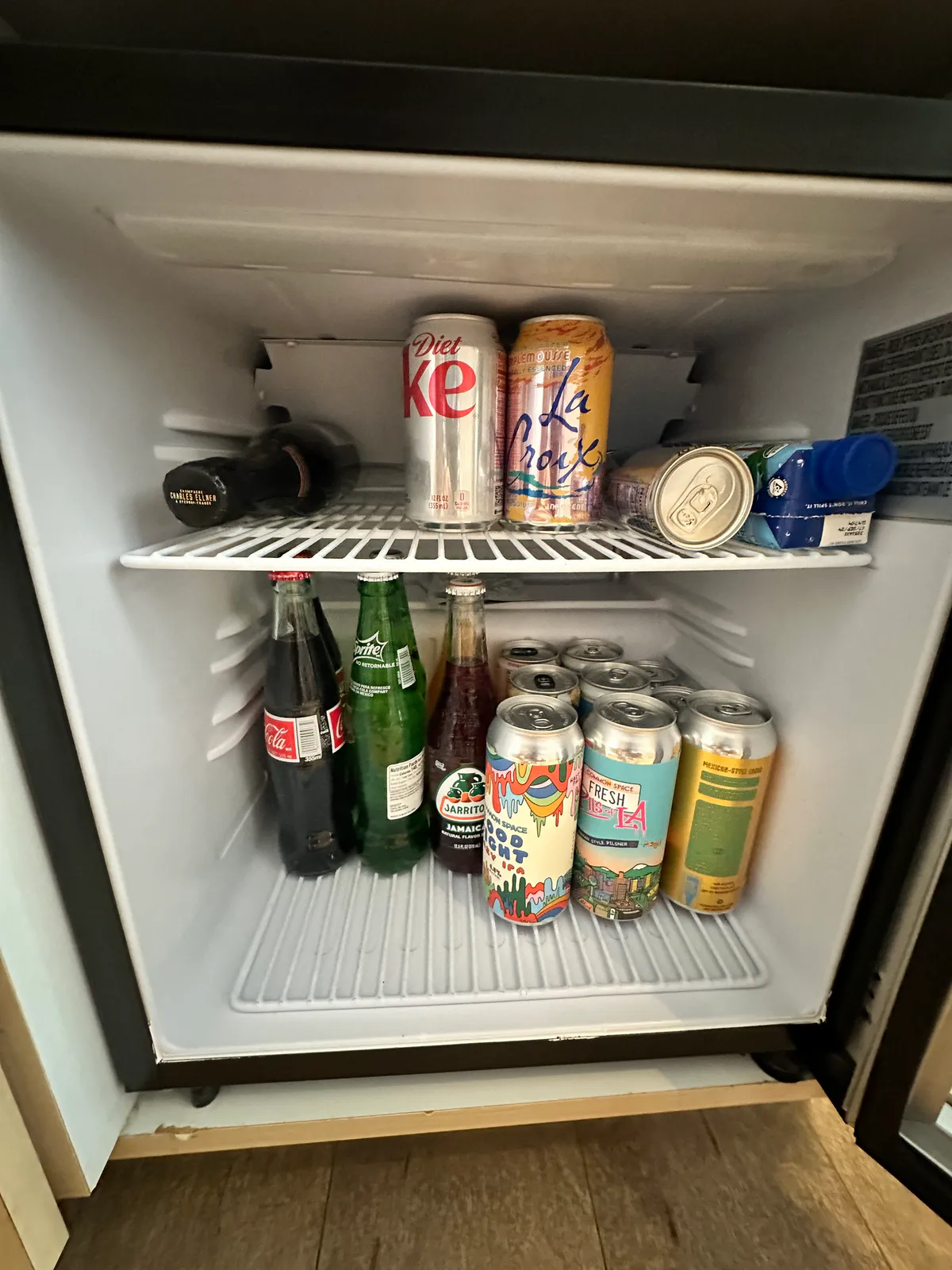 Open minifridge filled with soda bottles and cans on two wire shelves