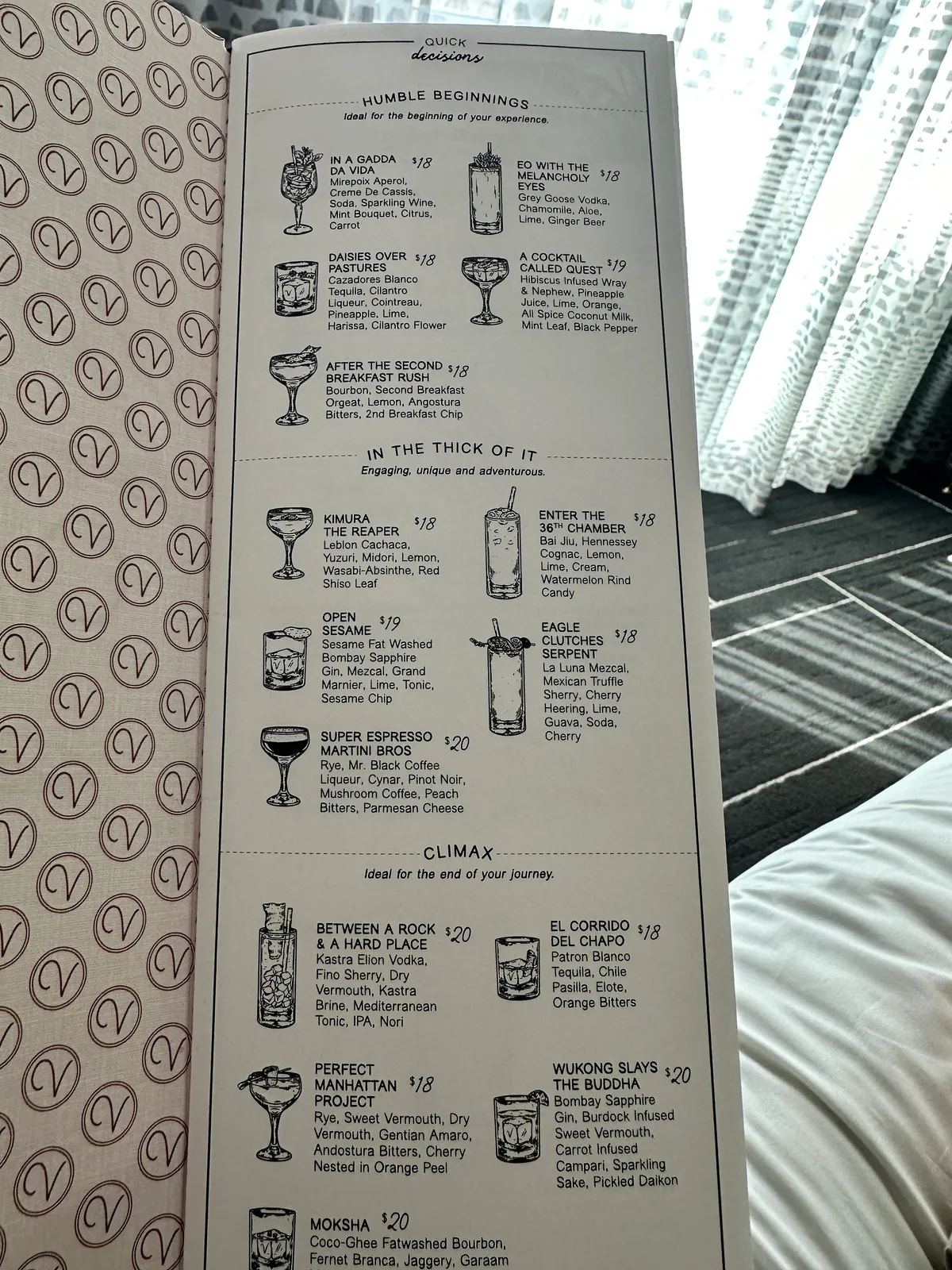 Open illustrated cocktail menu with drink drawings resting on white bedding