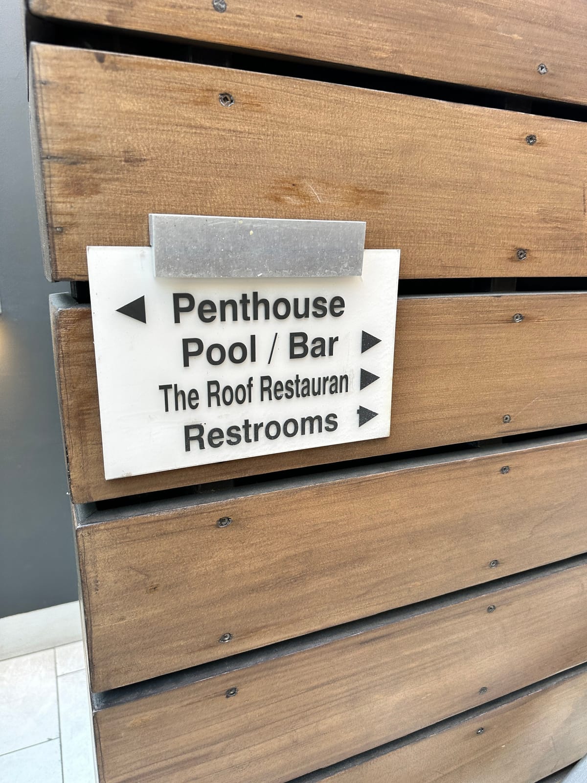 Wood-slat sign pointing to the penthouse, pool, roof restaurant, and restrooms