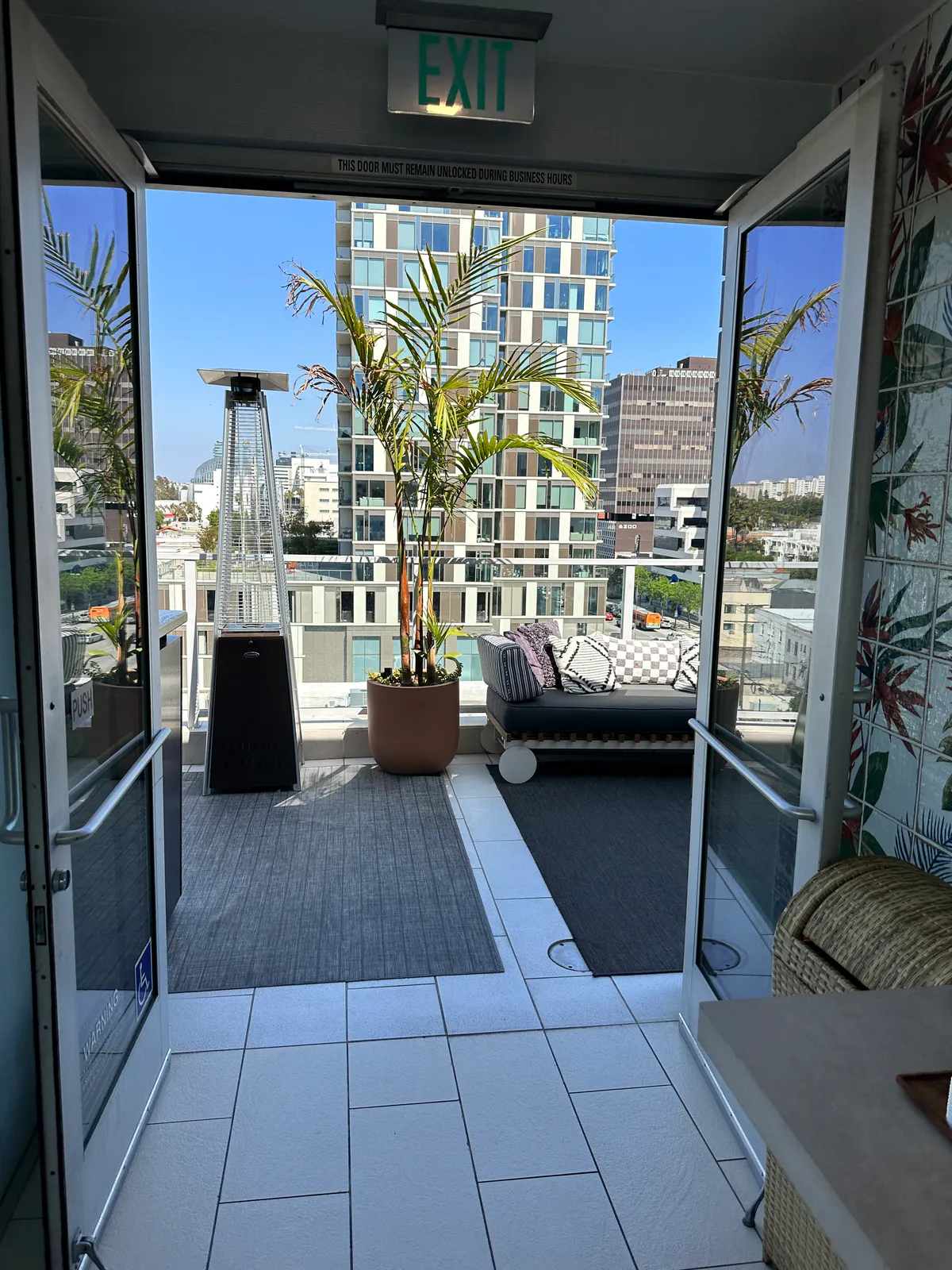 Open terrace doors framing a palm, patio heater, sofa, and city towers