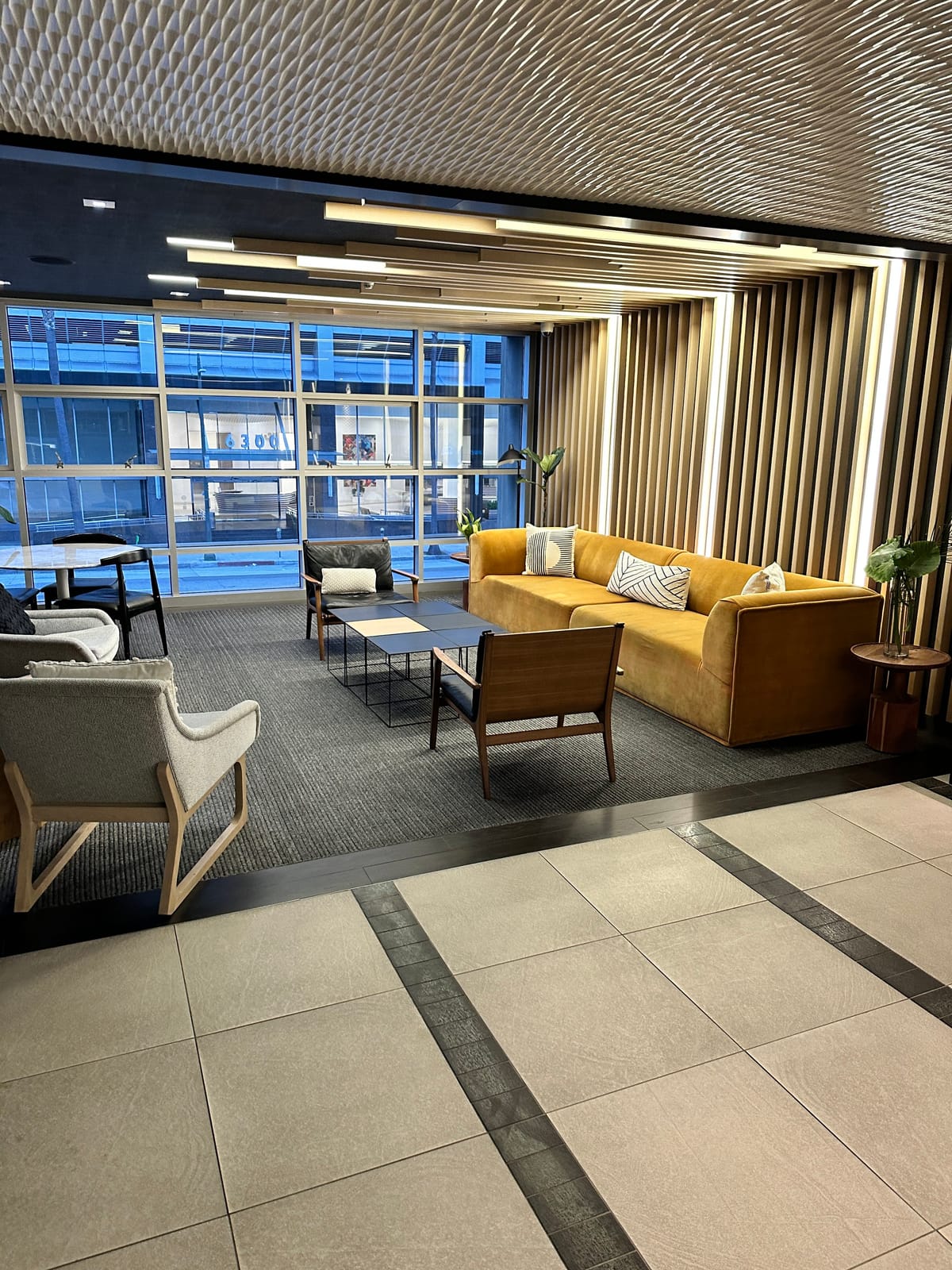 Seating lounge with a mustard sofa, wood slats, and tall blue-tinted windows
