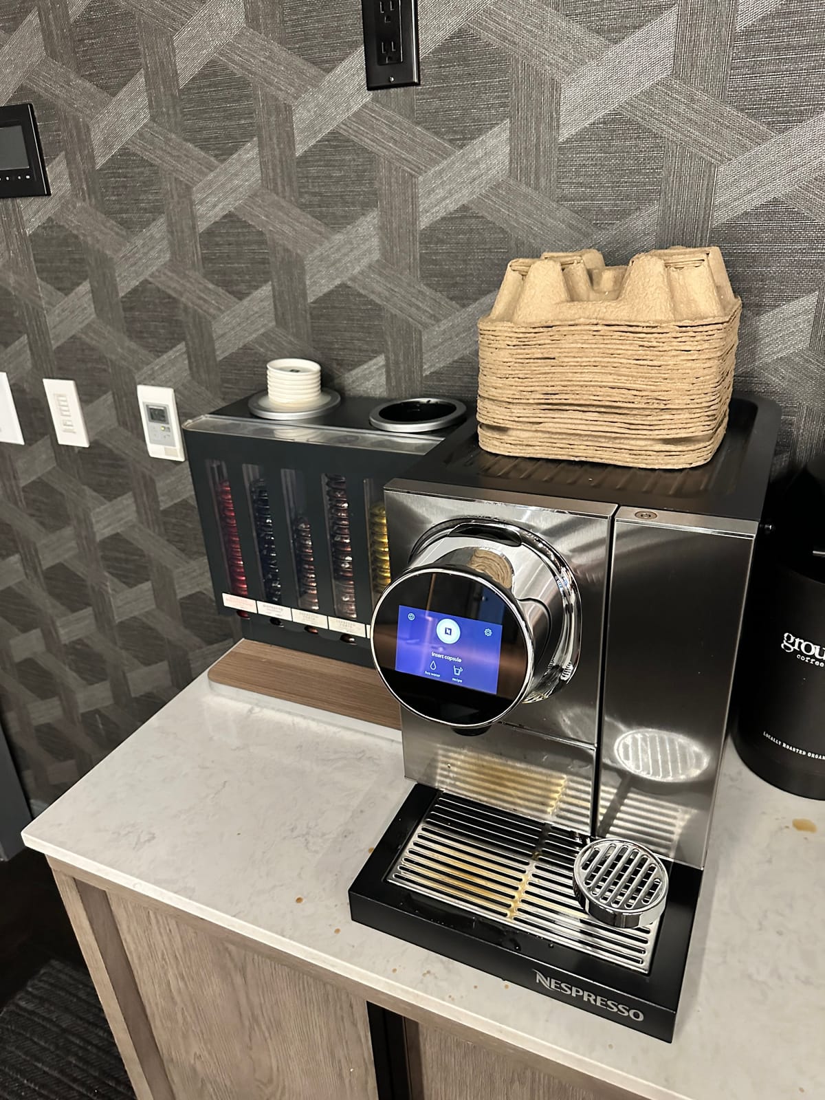 Front of a stainless Nespresso machine with capsules and a basket on top