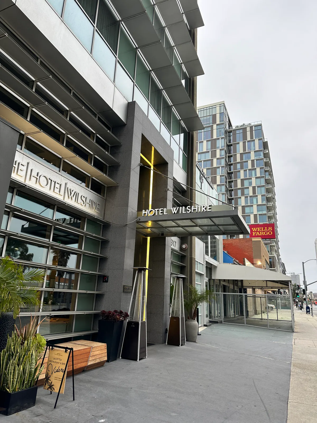 Glass hotel entrance canopy along the sidewalk with plants and patio heaters