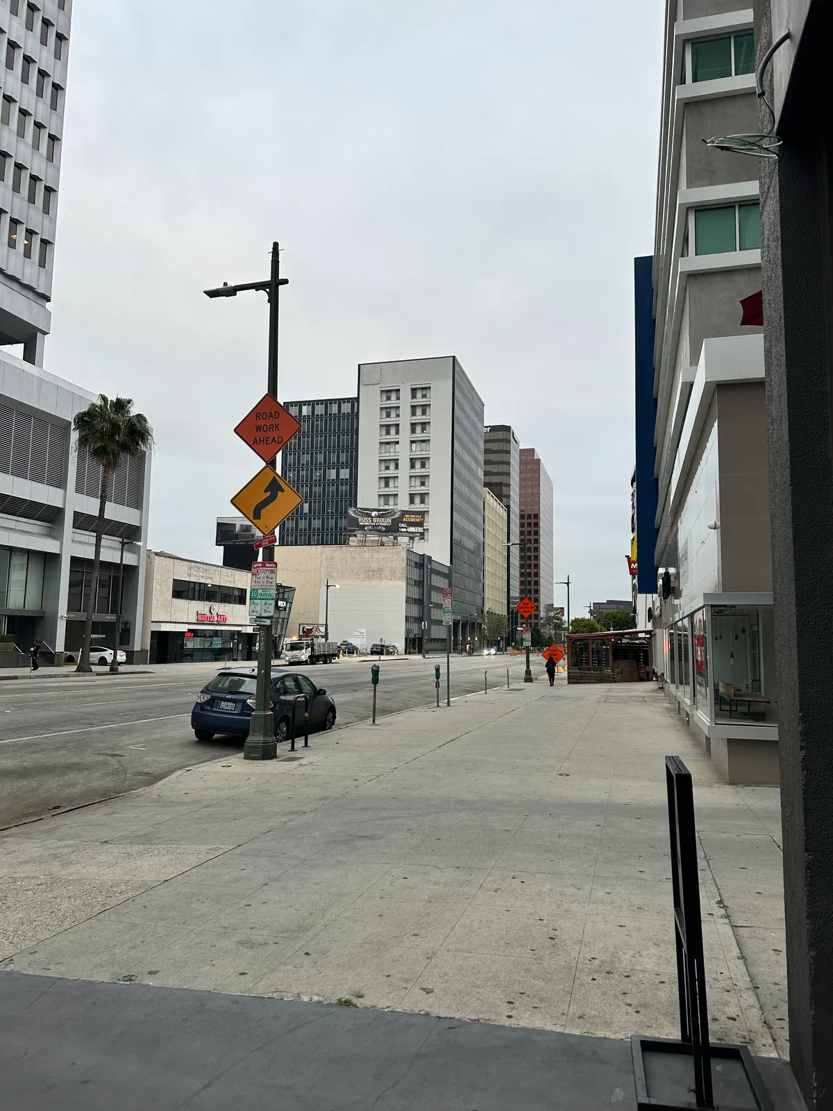 Sidewalk looking down a wide city street with road work signs and towers