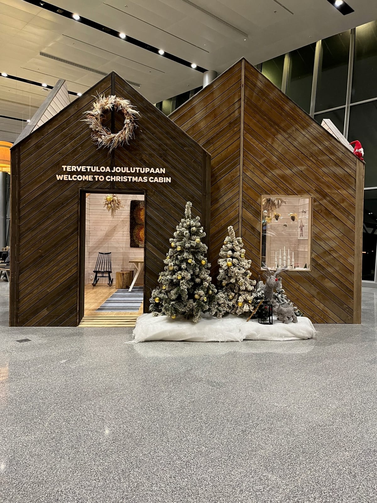 A wooden Christmas cabin display with flocked trees and a wreath in the terminal