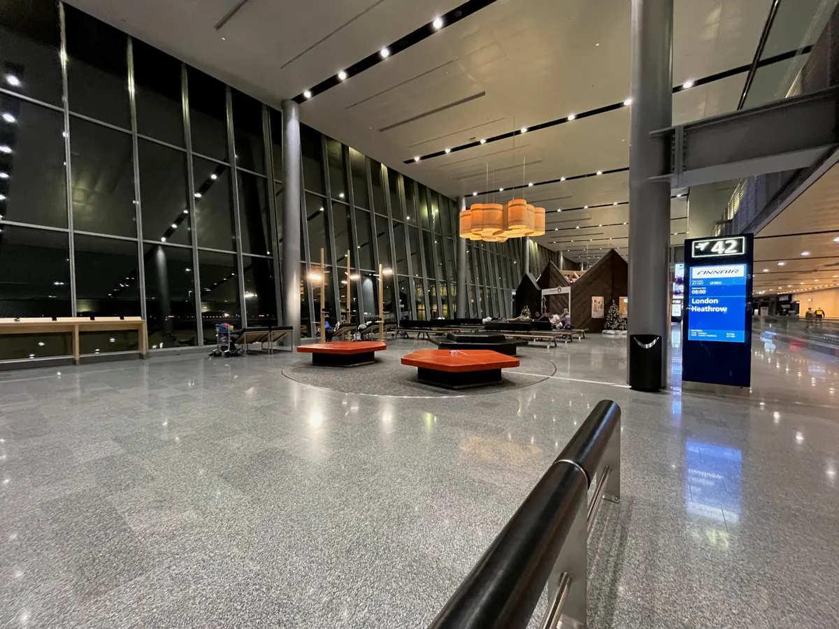Orange benches in a windowed gate hall beside a Finnair screen for London Heathrow