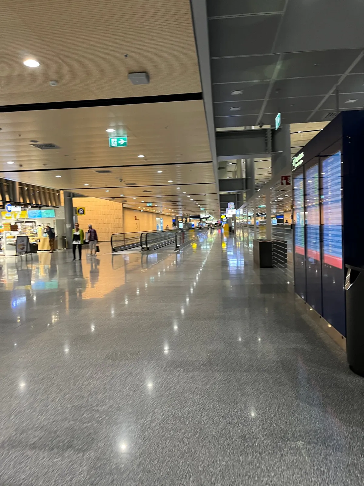 A nearly empty terminal corridor with a polished floor and flight information screens