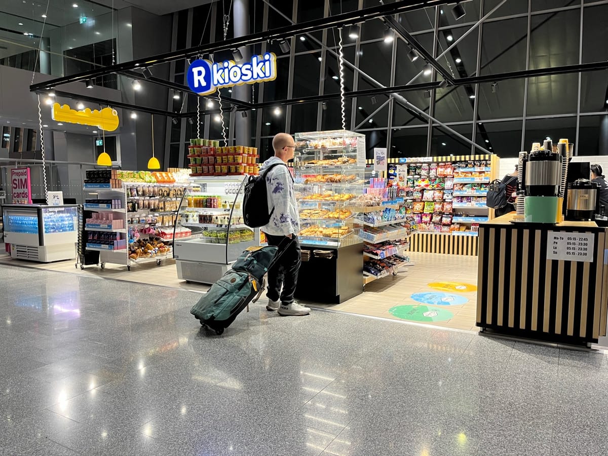 A traveler with a rolling bag browsing the pastry case at an R-kioski shop