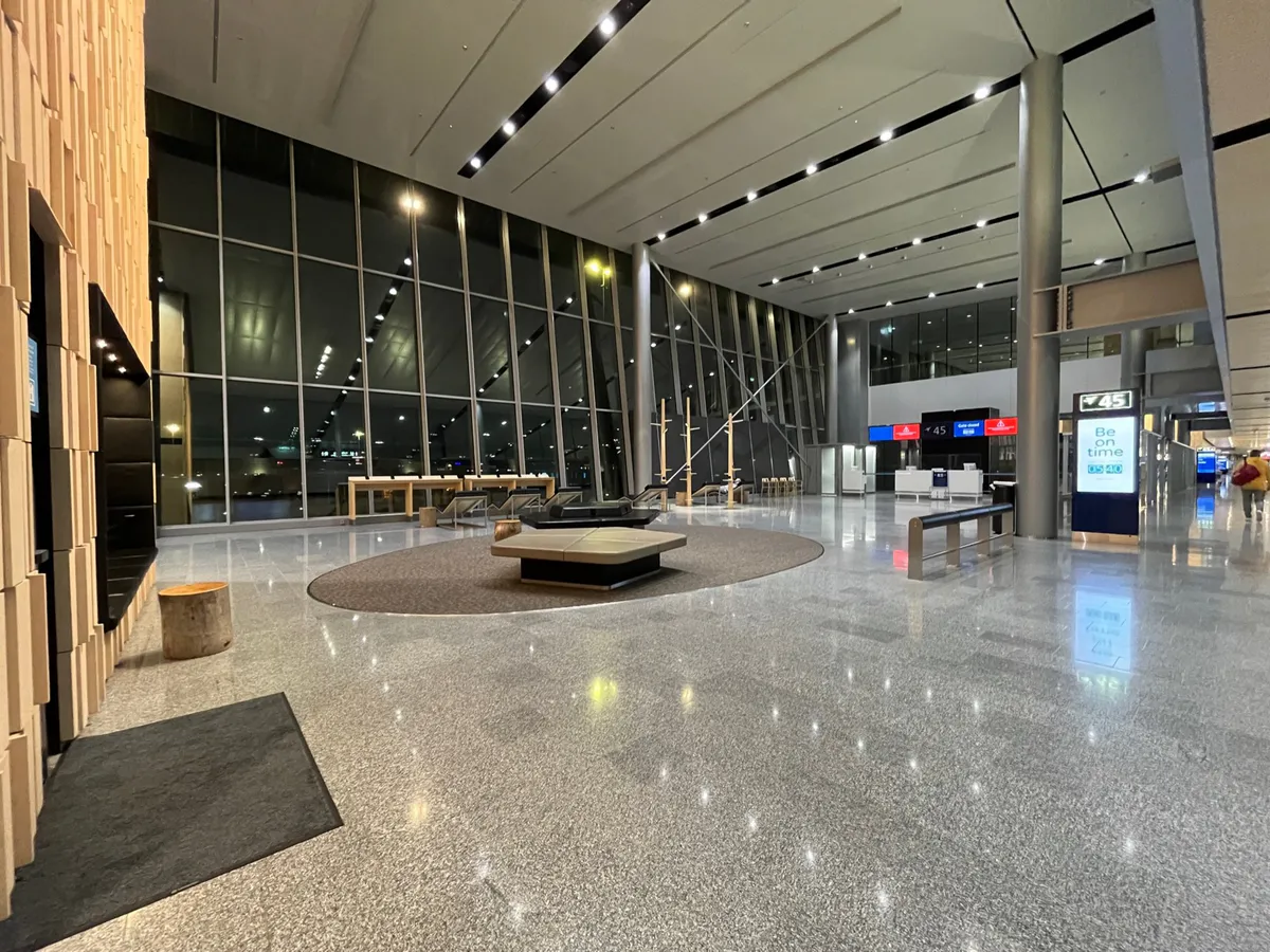 A spacious gate lounge at night with tall windows, an oval rug, and low seating