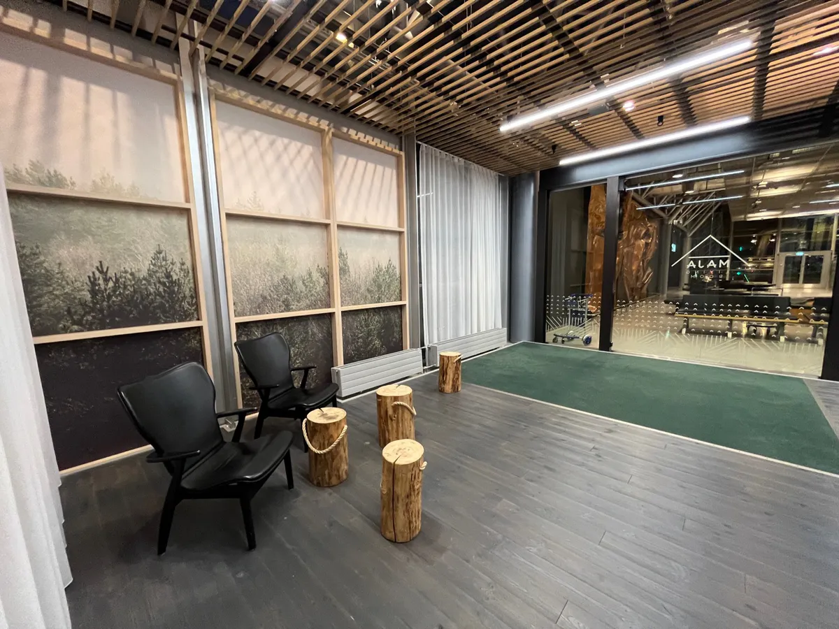 Black lounge chairs and log-stump stools beside forest photo panels