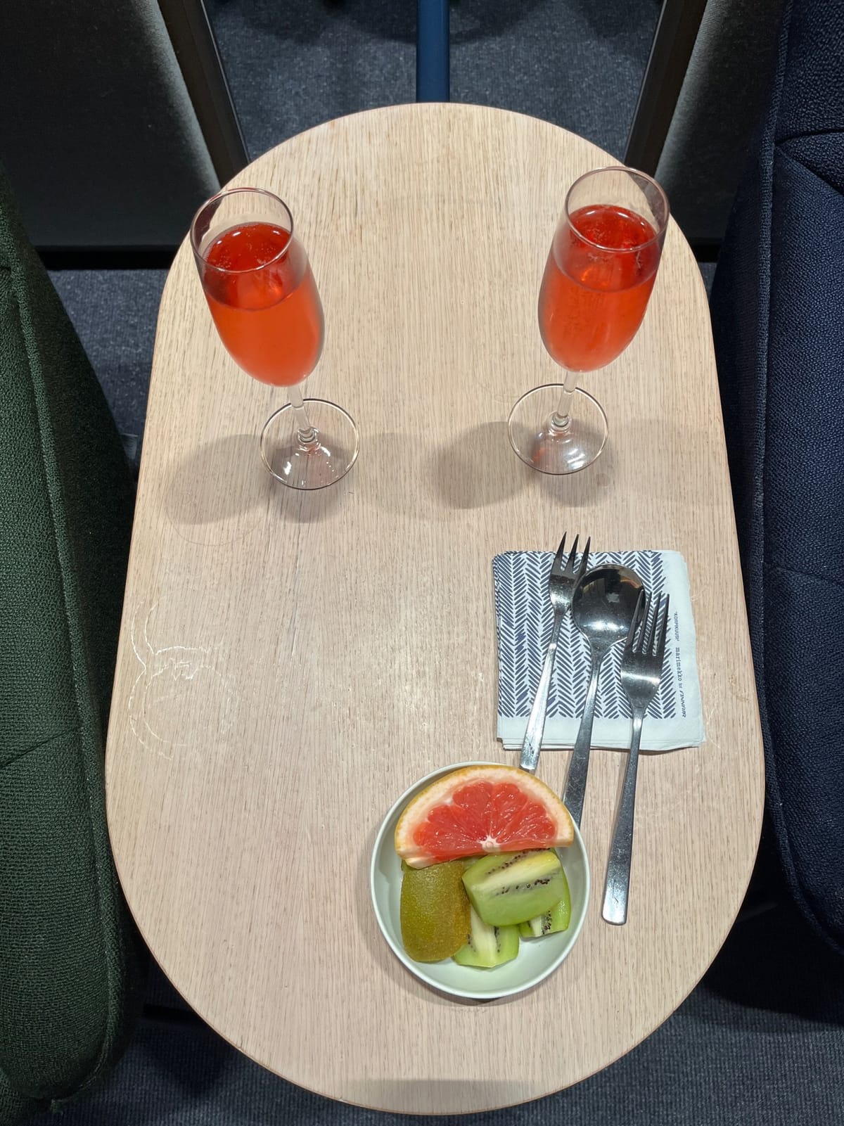 Two glasses of pink drink and a bowl of grapefruit and kiwi on a side table