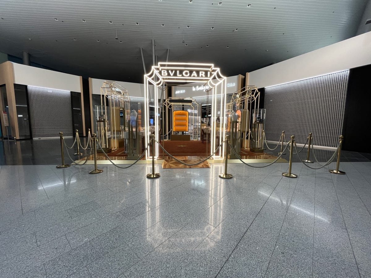 A lit BVLGARI display framed by gold rope barriers in a quiet terminal