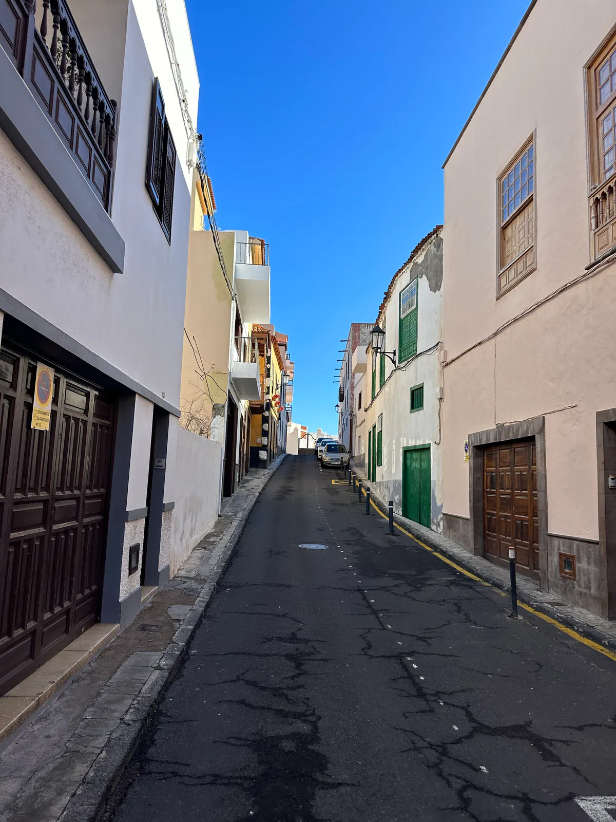 A narrow street climbing between white and peach houses with wooden doors.
