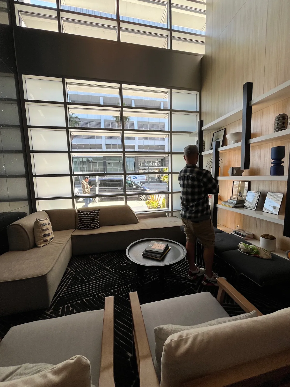 Lobby lounge with a beige sofa, books, and a man facing the window