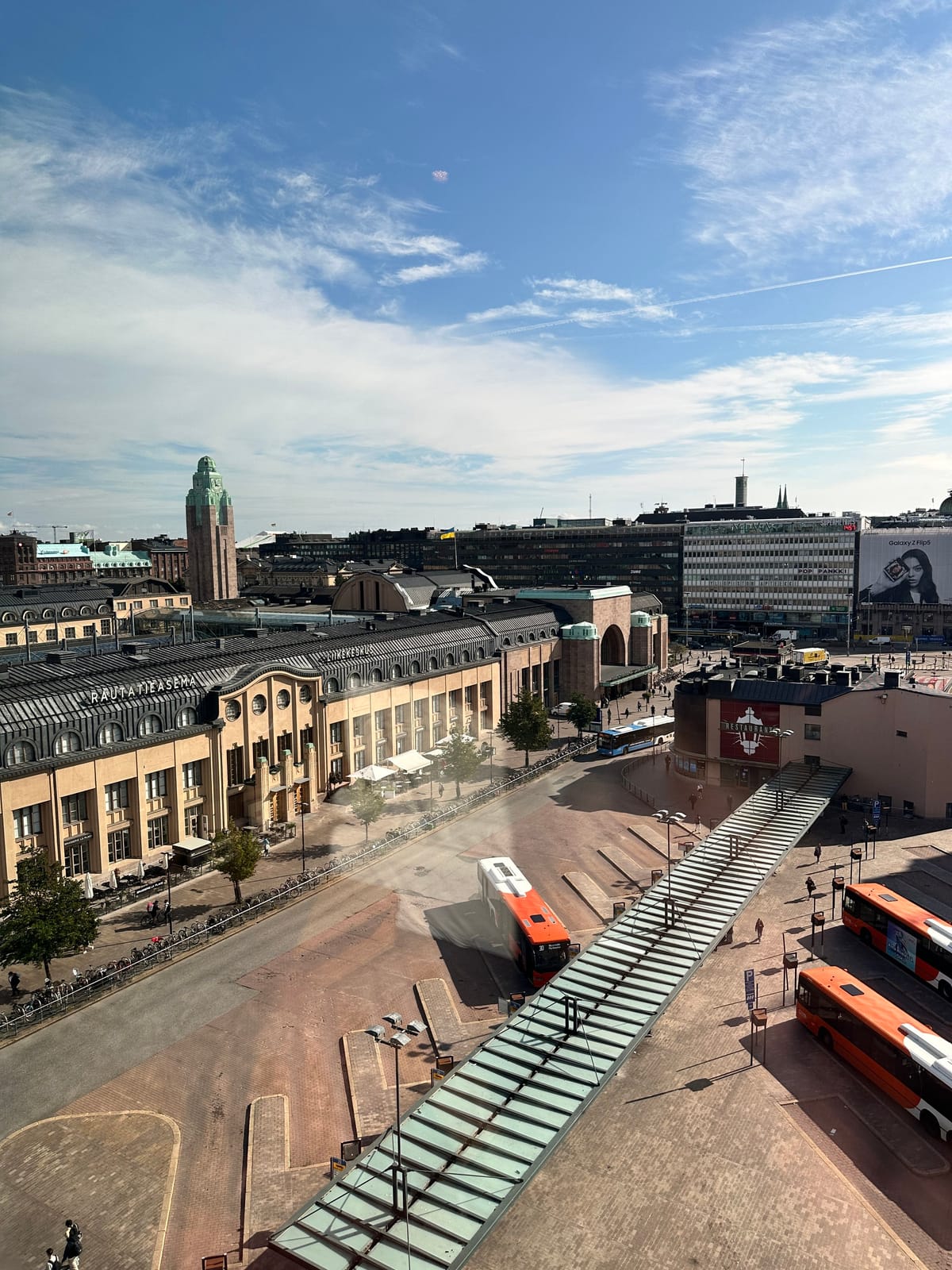 Holiday Inn view of Helsinki station, orange buses, and a glass walkway
