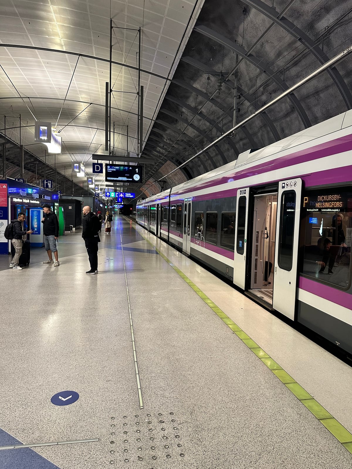 A white and magenta train stopped at an underground airport station platform