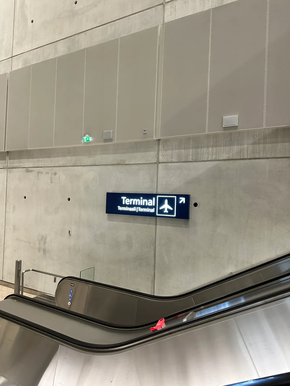 An escalator beneath a blue Terminal sign on a concrete wall