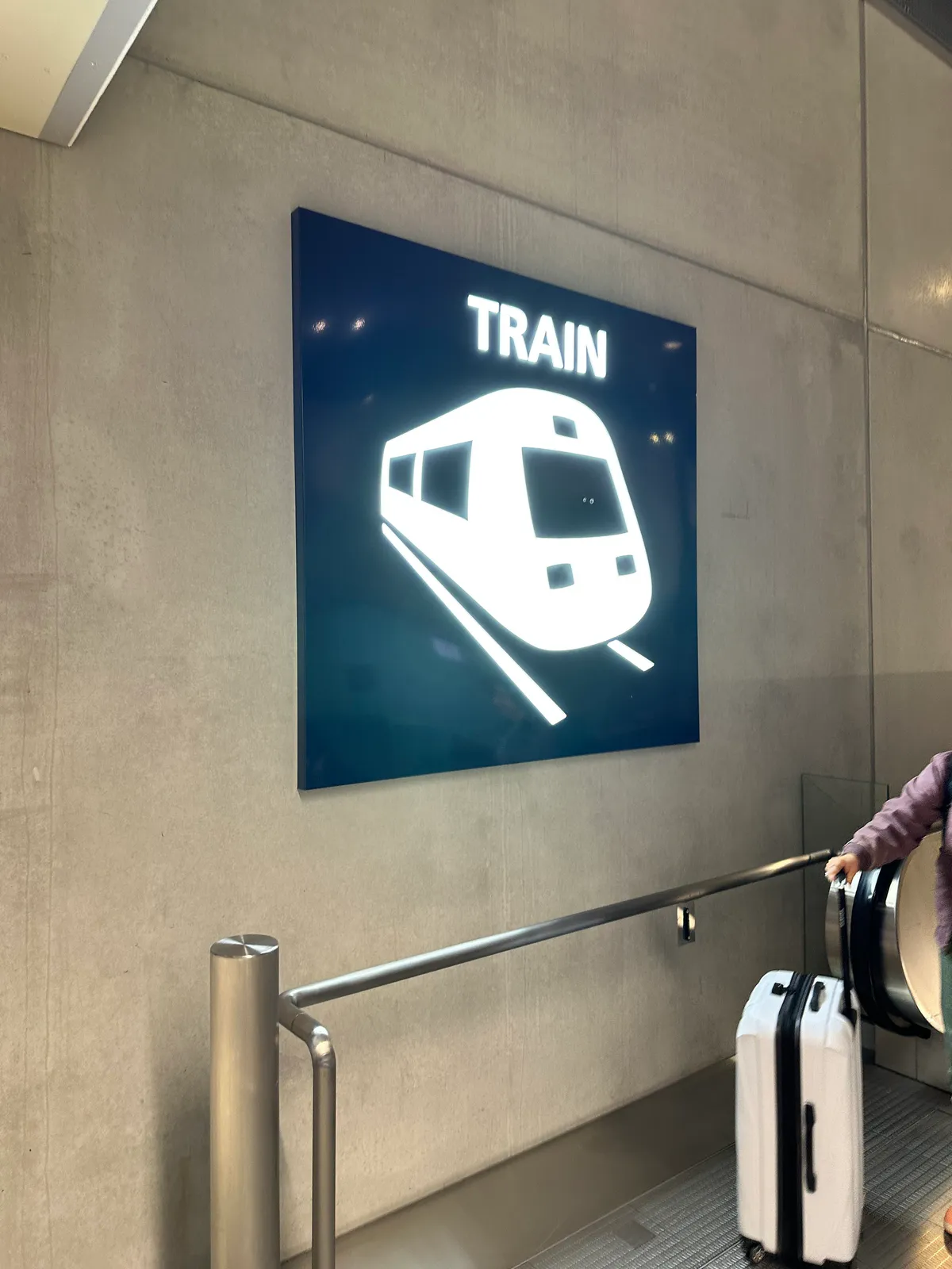 A glowing blue TRAIN sign above a traveler pulling a white suitcase