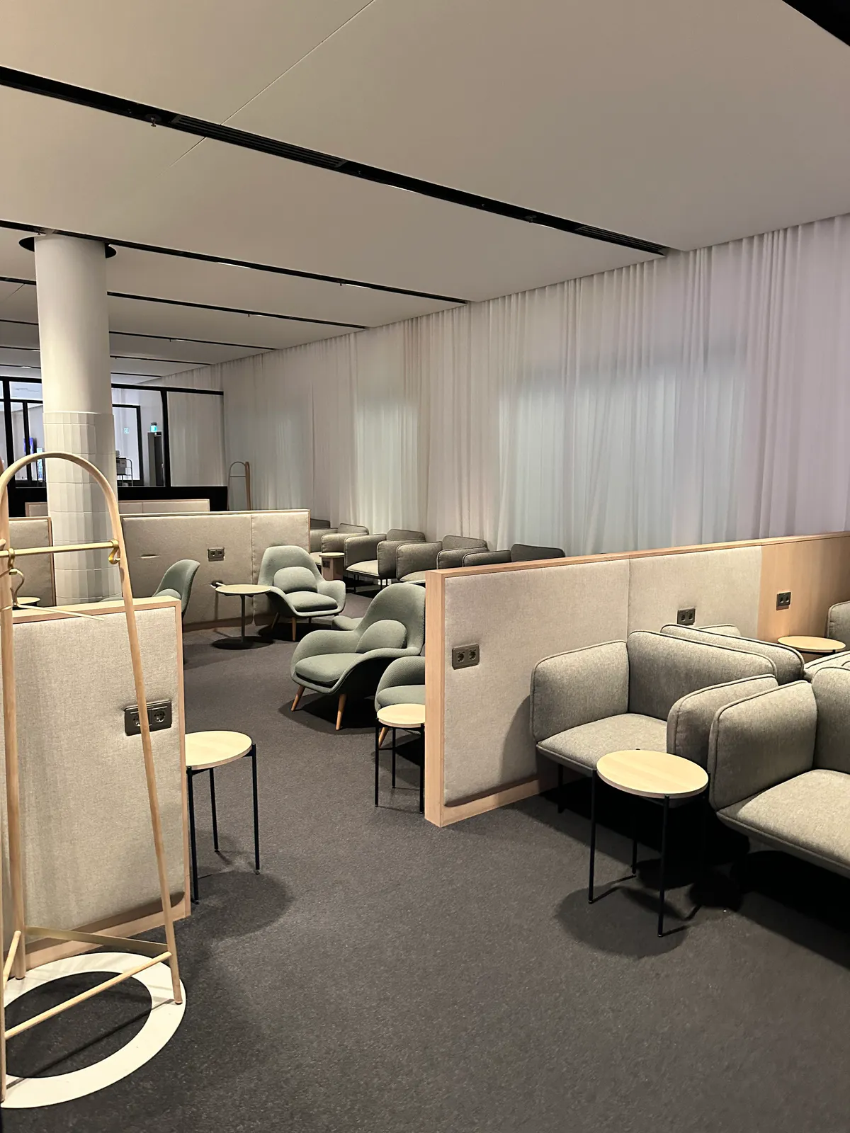 Gray sofas and sage armchairs divided by partitions beneath white curtains